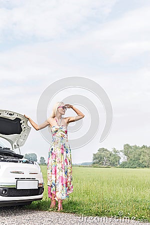 Woman shielding eyes while standing by broken down car on country road Stock Photo