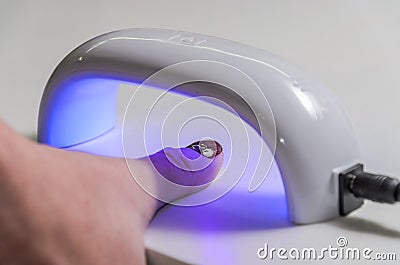 Woman shines with ultraviolet lamp on nails after manicure for nail polish to harden Stock Photo