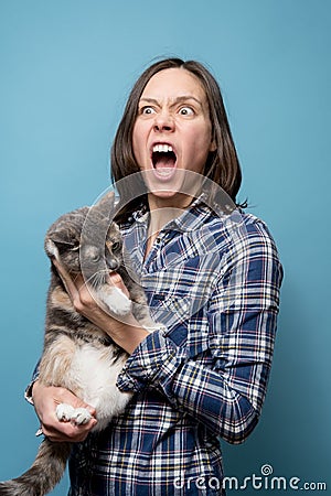 The woman is shocked and screams loudly, she is holding her beloved cat in her arms, which got angry and painfully bit Stock Photo