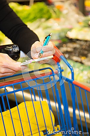 Woman is shopping at the supermarket detail of the cart and her hands at the shelf Stock Photo