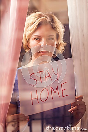 Woman staying in flat in front of window holding a sheet of paper with title stay home. People and healthcare concept Stock Photo