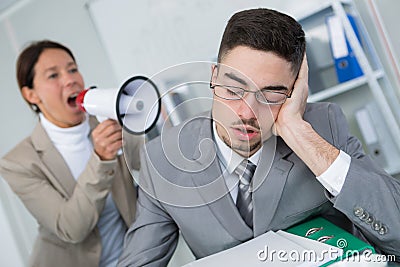 Woman shouting through loudhailer at sleepy office worker Stock Photo