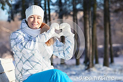 Woman showing heart shape with white mittens in sunlight at winter Stock Photo