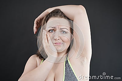 Unhappy woman shows her unshaved armpit. plus size middle age woman is not happy with hair in her armpits. Caucasian girl is Stock Photo