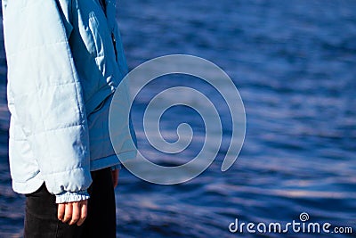 Woman side view in a jacket on a background of blue water. Copy space. Melancholy mood Stock Photo