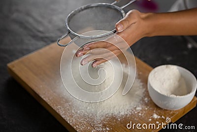 Woman sieving flour from the bowl on the wooden board Stock Photo