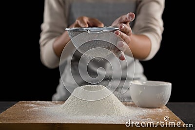 Woman sieving flour from the bowl on the wooden board Stock Photo