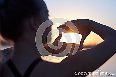 Woman silhouette framing sun with fingers at sunset. Hand shape of a camera across the sky Stock Photo