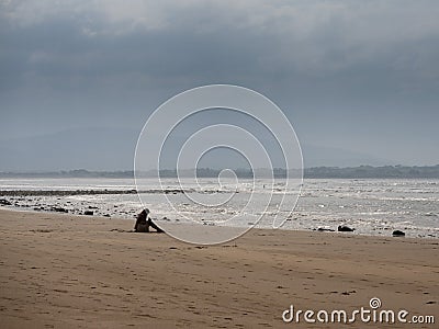 Woman siting on a beach, concept relaxing listening to oceans wave noise. Silverstrand beach, Ireland. Peacefull and relaxing Stock Photo