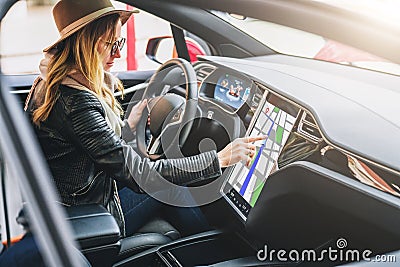 Woman sits behind wheel in car and uses electronic dashboard. Girl traveler looking for way through navigation system. Stock Photo