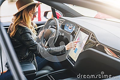 Woman sits behind wheel in car and uses electronic dashboard. Girl traveler looking for way through navigation system. Stock Photo