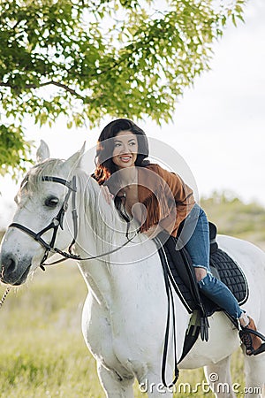 Woman sits horseback on white horse on meadow Stock Photo