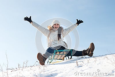 Woman sits and sledges from the mountain against the background of snow and sky in winterGirl laughs and rejoices in snow, Stock Photo