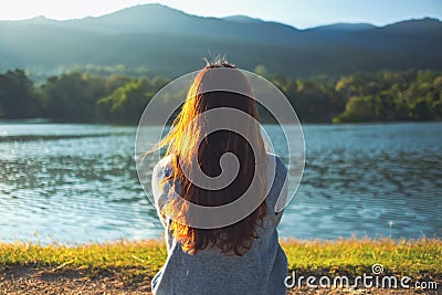 A woman sitting alone by the lake looking at the mountains with green nature Stock Photo