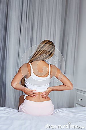 Woman sitting on a bed with back pain Stock Photo