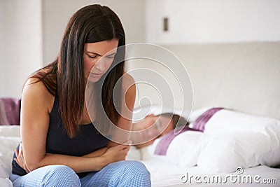 Woman Sitting On Bed And Feeling Unwell Stock Photo
