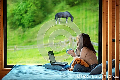 Woman sitting on the bed and looks outside the window seeing mountain. Stock Photo