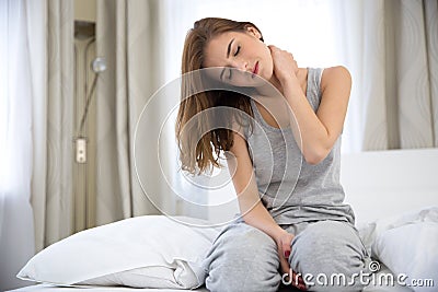 Woman sitting on the bed with pain in neck Stock Photo