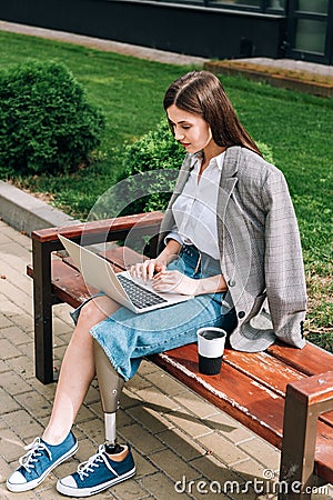 Woman sitting on bench and using laptop on street Stock Photo