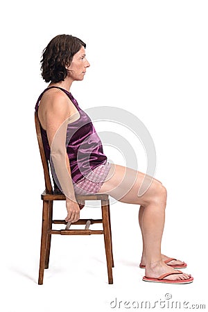 Woman sitting on a chair dressed in a short summer pajamas on white background,side wiew Stock Photo
