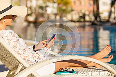 Woman sitting in chair by the swimming pool and using smartphone Stock Photo