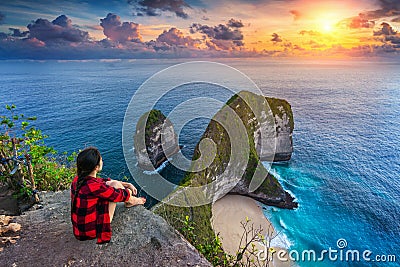 Woman sitting on cliff and looking at sunset at Kelingking Beach in Nusa penida island, Bali, Indonesia. Stock Photo