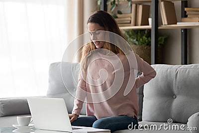 Woman sitting on couch near laptop suffers from back pain Stock Photo