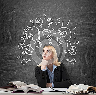 Woman sitting at the desk with books around thinking education Stock Photo