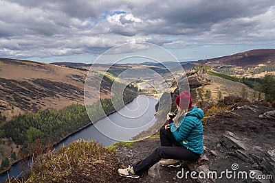 Woman sitting on the edge of a cliff, enjoying the landscape. Glendalough, Wicklow, Ireland. Stock Photo