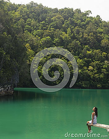 A woman sitting on the edge of a diving board in a magnificent green lagoon. Stock Photo