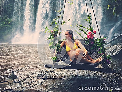 Woman sitting in flowered swing near waterfall, Phnom Koulen at Siem Reap, Cambodia Stock Photo