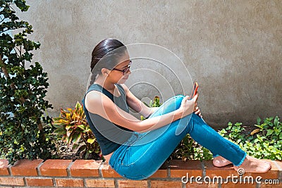 A woman is sitting in the garden checking her cell phone Stock Photo