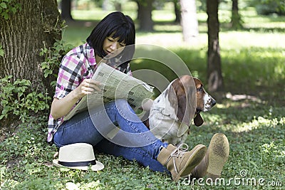 Woman sitting in the grass in the park reading the newspaper and Stock Photo