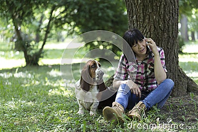 Woman sitting in the grass in the park talking on the mobile phone and relaxing with her dear dogs Stock Photo