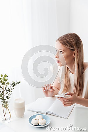 Woman sitting indoors near sweeties holding mobile phone. Stock Photo