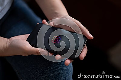 A woman sitting indoors and using a Instagram application through her Iphone14. An Instagram logo Editorial Stock Photo