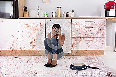 Woman Sitting On Kitchen Floor With Spilled Food Stock Photo