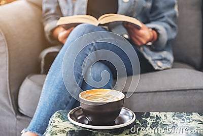 A woman sitting and reading a vintage novel book on sofa with coffee cup on the table Stock Photo