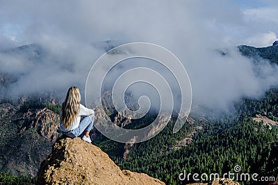 Woman sitting on a rock with the amazing view of Roque Nublo in Gran Canaria Stock Photo