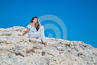 Woman sitting on rock and looking away. Relaxing moment and dreaming. Feeling of calm. Contemplation and comprehension. Stock Photo