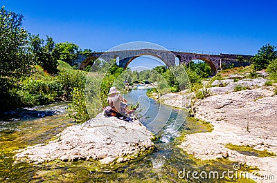 Woman sitting on the rock and painting roman bridge Pont Julien in Provence Editorial Stock Photo
