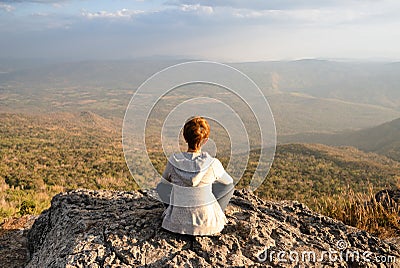 A woman sitting on rocky mountain looking out at scenic natural view and beautiful blue sky Stock Photo