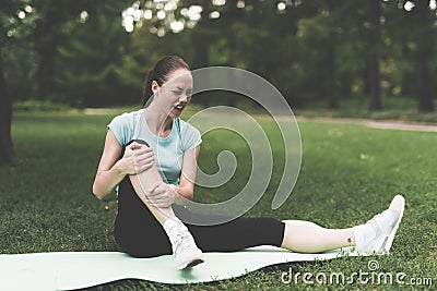 A woman is sitting on a rug for yoga in the park. She was engaged and traumatized her leg. Stock Photo