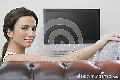 Woman Sitting On Sofa With Flat Screen TV In Background Stock Photo