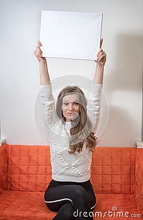 Woman sitting on a sofa and holding outstretched empty sheet of paper with copy spac Stock Photo