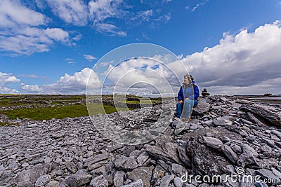 Woman sitting on the stones of the rocky beach of Inis Oirr Island Stock Photo
