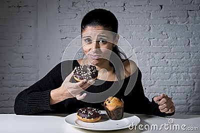 Woman sitting at table feeling guilty forgetting diet eating dish full of junk sugary unhealthy food Stock Photo