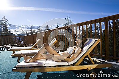 Woman sitting on a terrace in bikini in the snowy mountains Stock Photo
