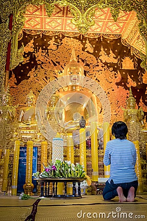 A woman is sitting to pray in front of golden Buddha statue of Thailand temple named `Wat Den Salee Sri Muang Gan Wat Ban Den`. Editorial Stock Photo