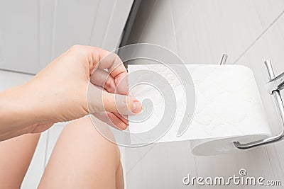 Woman sitting on a toilet in a restroom and rips off a piece of toilet paper from a roll, digestive problems and defecation Stock Photo